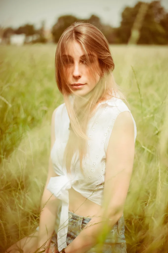 La modella è in un campo di erba alta, i fili d'erba sfocati in primissimo piano danno un idea di profondità senza interferire col soggetto.